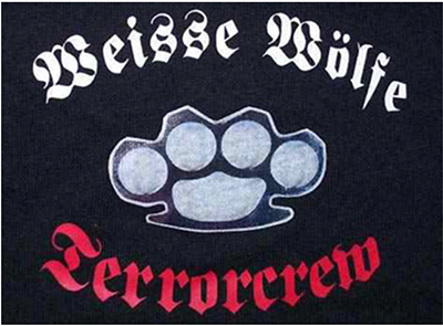 In einem Oval angeordnet der Schriftzug „Weisse Wölfe“ in altdeutscher weißer Schrift auf schwarzem Grund, darunter ein großer stilisierter Schlagring, darunter das Wort „Terrorcrew“ in altdeutscher roter Schrift.
