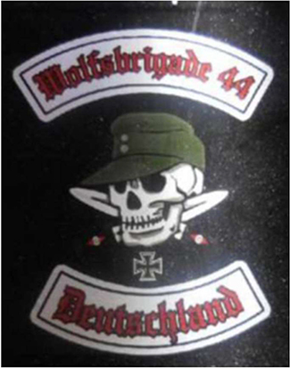 Totenschädel kombiniert mit olivfarbener Feldmütze vor zwei gekreuzten Dolchen, einem eisernen Kreuz sowie roter Beschriftung in gebrochener Schrift mit schwarzer Umrandung auf weißen Bannern „Wolfsbrigade 44“ und „Deutschland“
